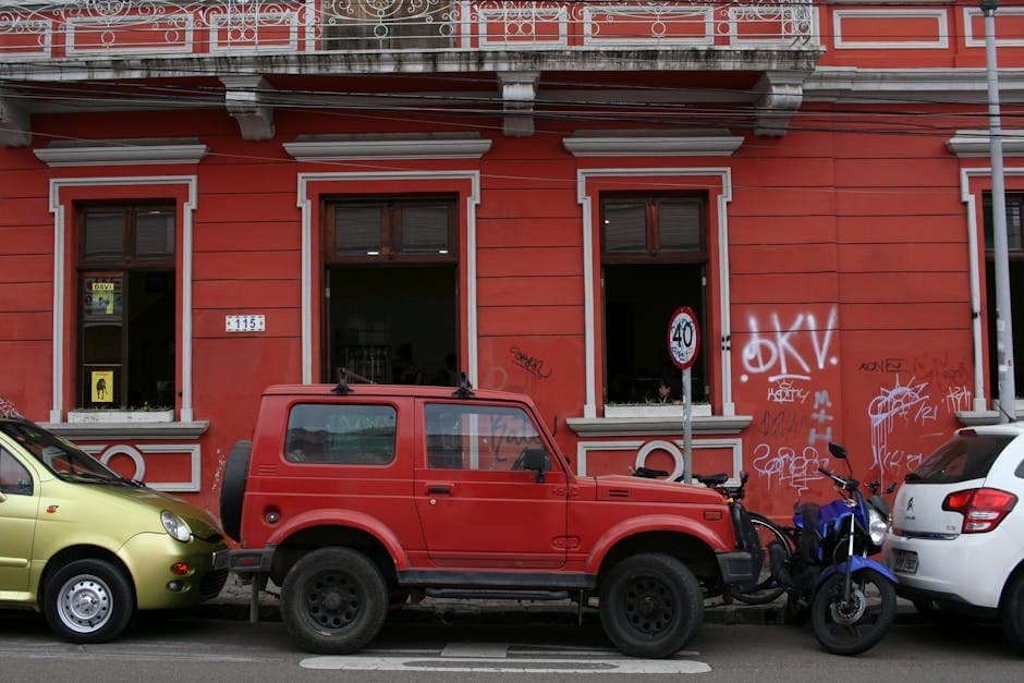 Street scene in Curitiba with parked cars and motorbike against a red building.