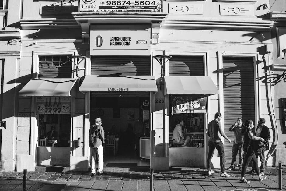 Monochrome image of pedestrians outside a café in a bustling urban street.