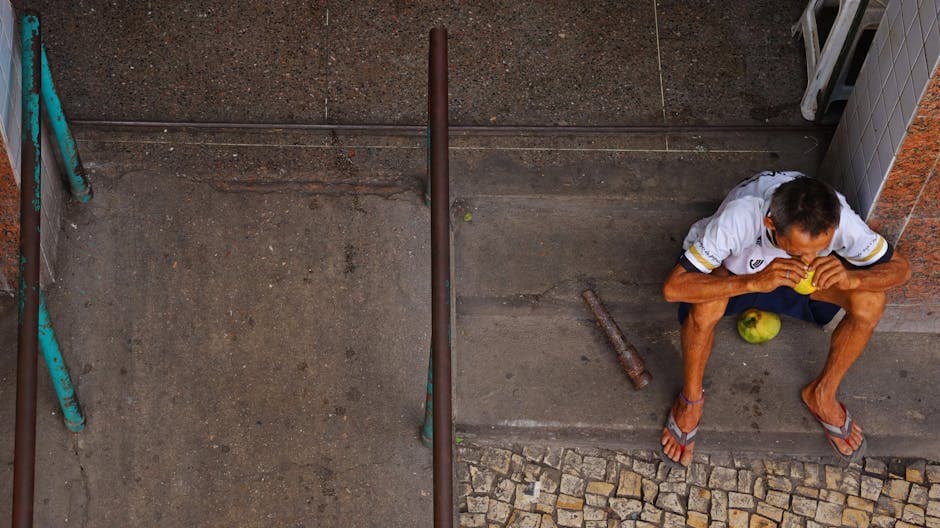 A man sitting on urban steps eating fruit, captured from above in Fortaleza, Brazil.