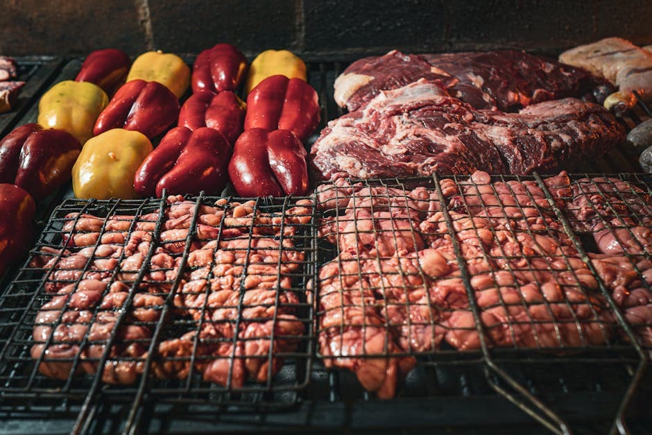 Assorted meats and peppers being grilled over charcoal, capturing a rustic barbecue experience.