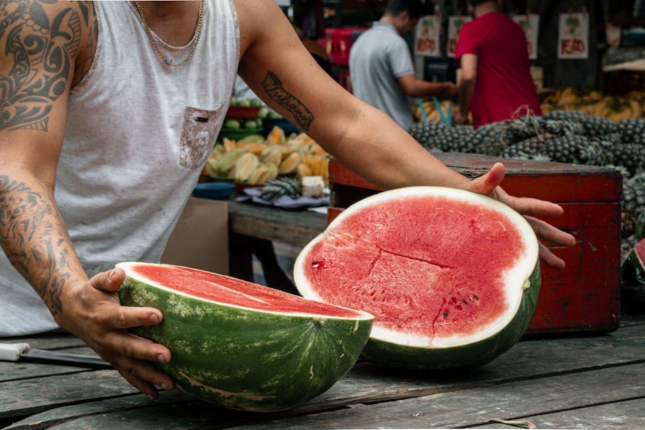 Tattooed vendor displaying sliced watermelon at vibrant São Paulo market.