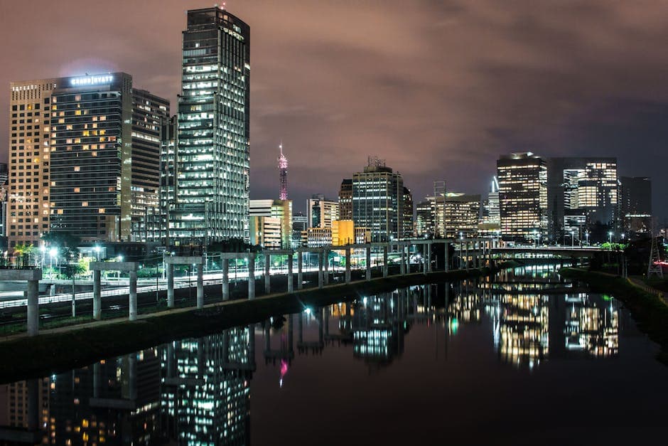 Illuminated cityscape of São Paulo reflecting in water at night. Modern architecture with a dramatic sky.