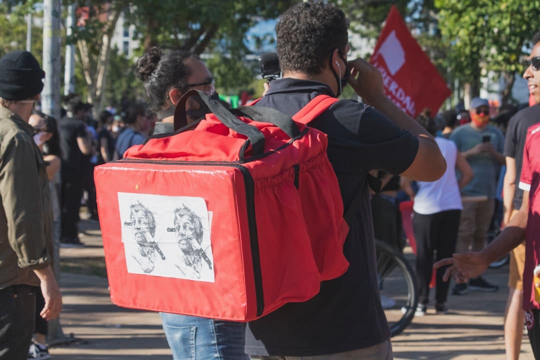 man in red and black backpack walking on sidewalk during daytime