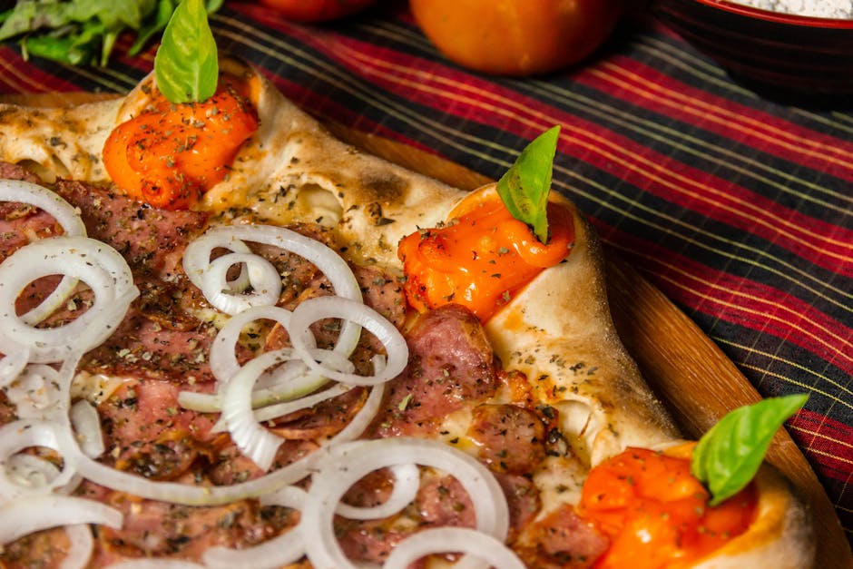 Delicious gourmet pizza with fresh onions, bell peppers, and basil leaves.
