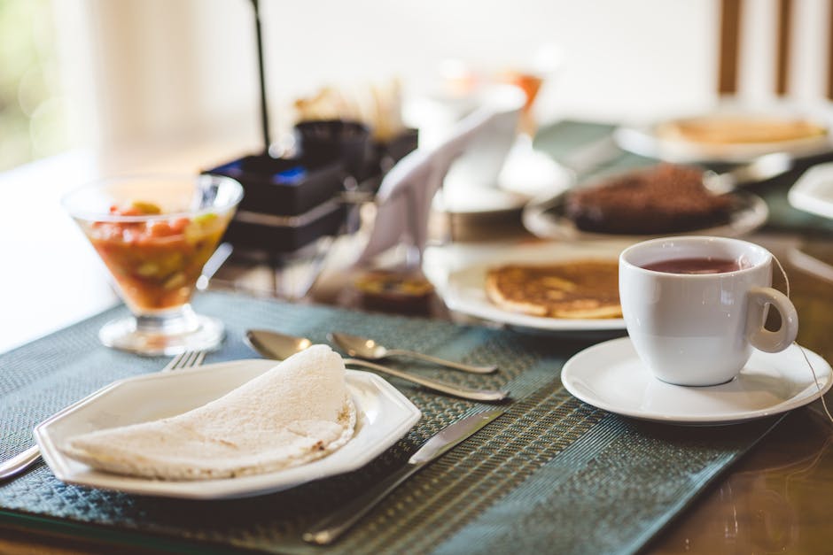 A cozy breakfast setting featuring tea, crêpes, and fruit salad on a neatly arranged table indoors.