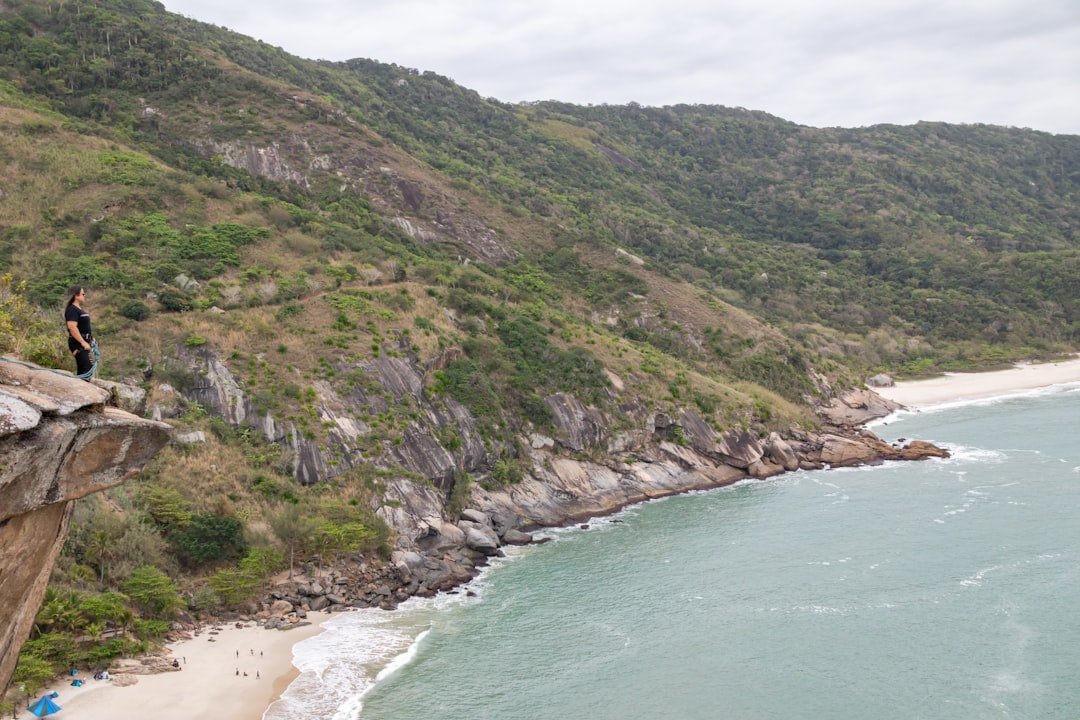 a person standing on a cliff above a beach and water