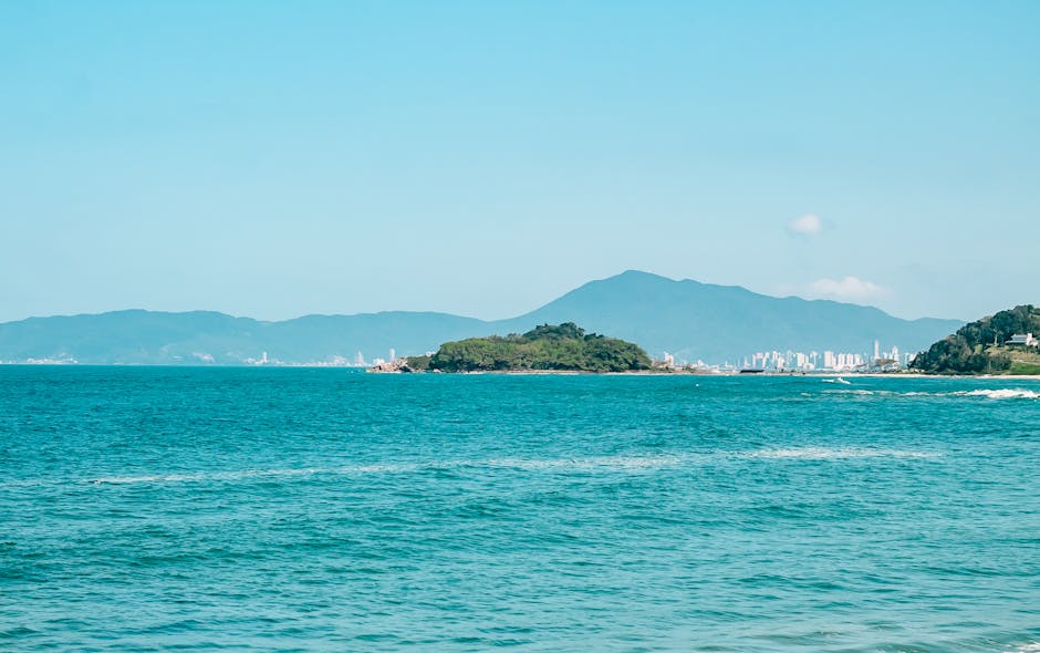 Beautiful seascape with clear blue waters, an island, and a distant city under a bright summer sky.