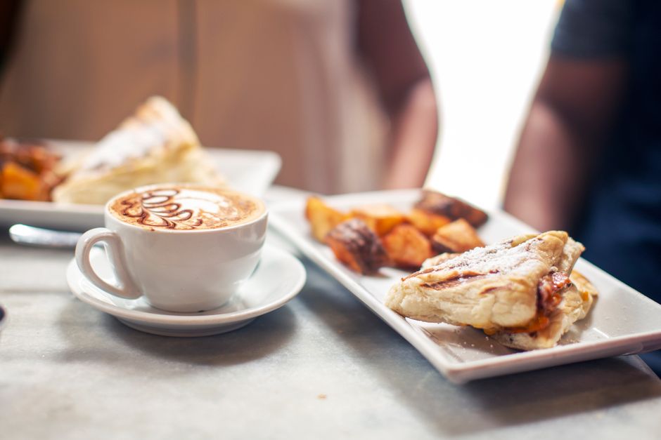 Dining table with delicious grilled sandwich and sweet potato served near freshly brewed cappuccino