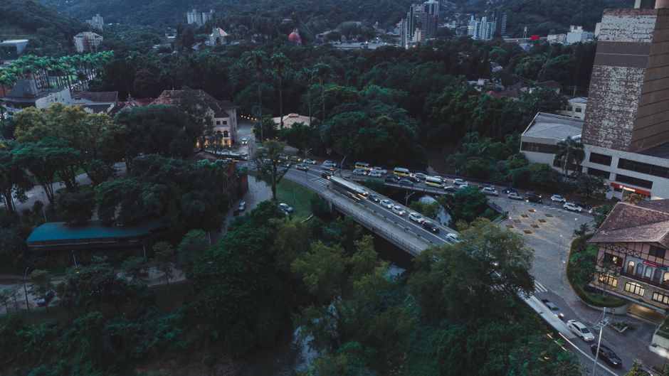 Aerial view of bustling street amid lush greenery in Blumenau, Brazil at dusk.