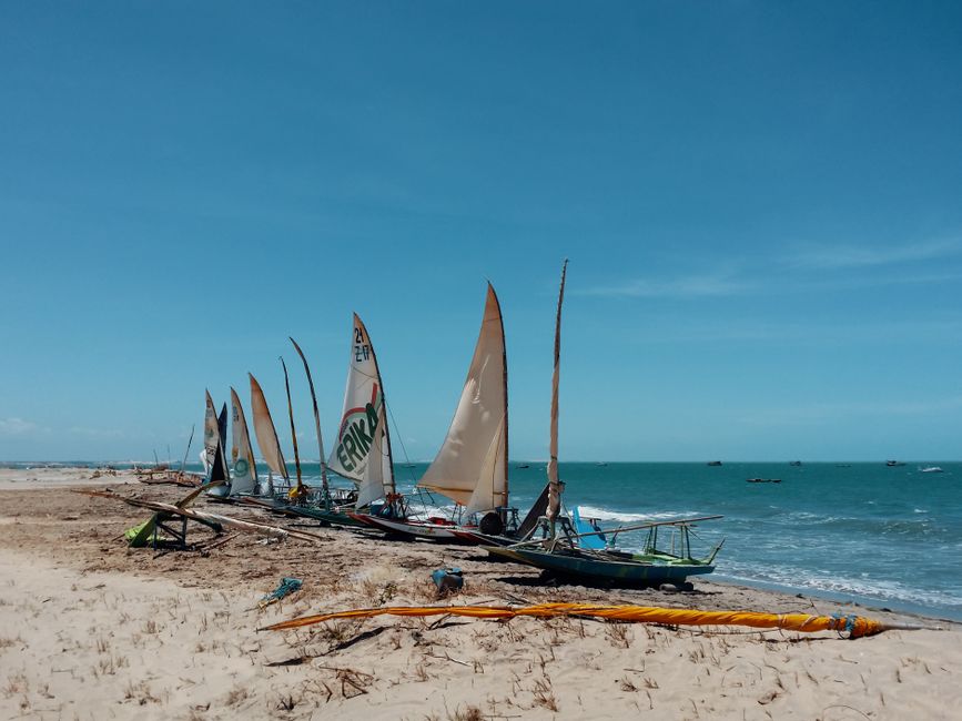 Colorful traditional sailboats lined up on the sandy shores of Canoa Quebrada, Brazil under clear blue skies.