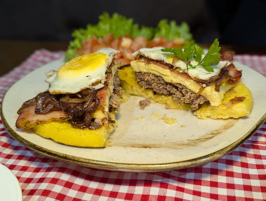 Mouthwatering Brazilian burger topped with fried egg, bacon, and cheese on a checkered tablecloth.