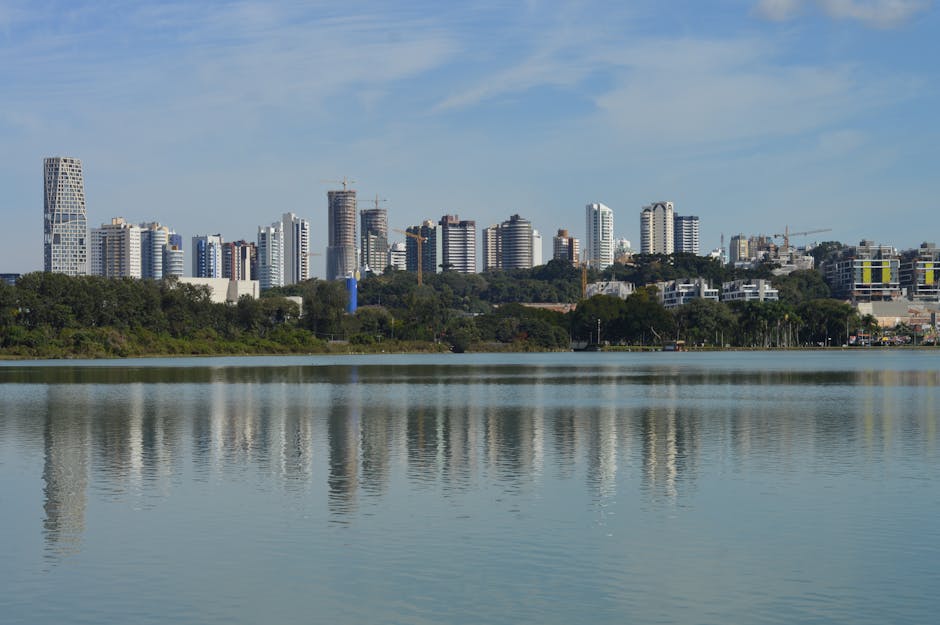 Skyline of Curitiba, Brazil, reflecting on a serene lake under a clear blue sky.