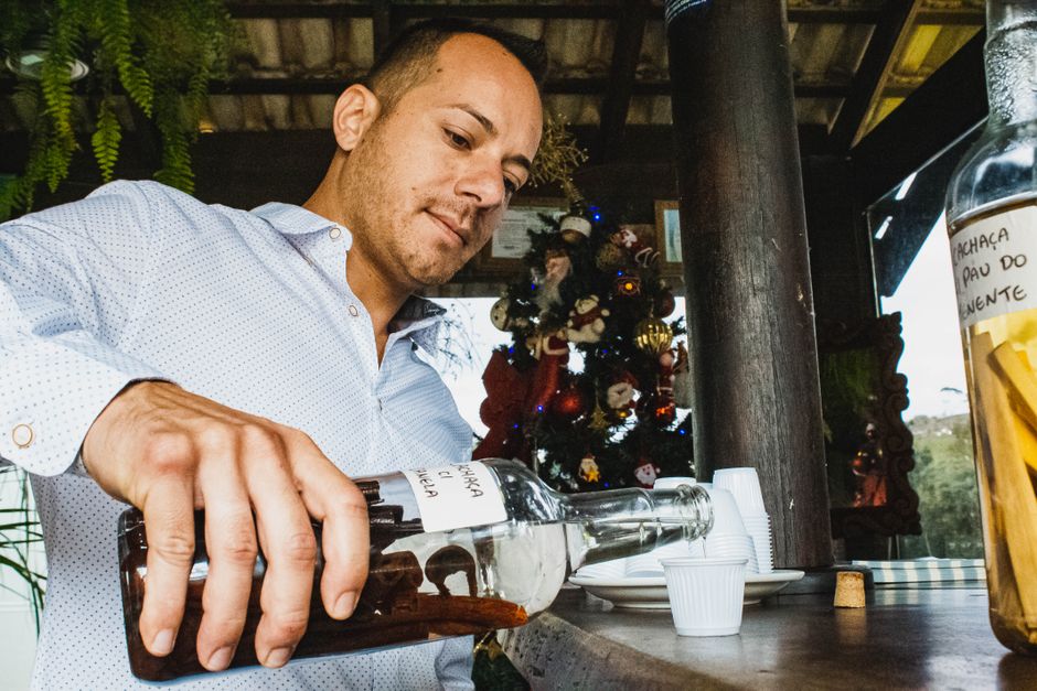 Low angle of young male in classic shirt pouring alcohol drink in shot sitting at wooden counter in summer bar