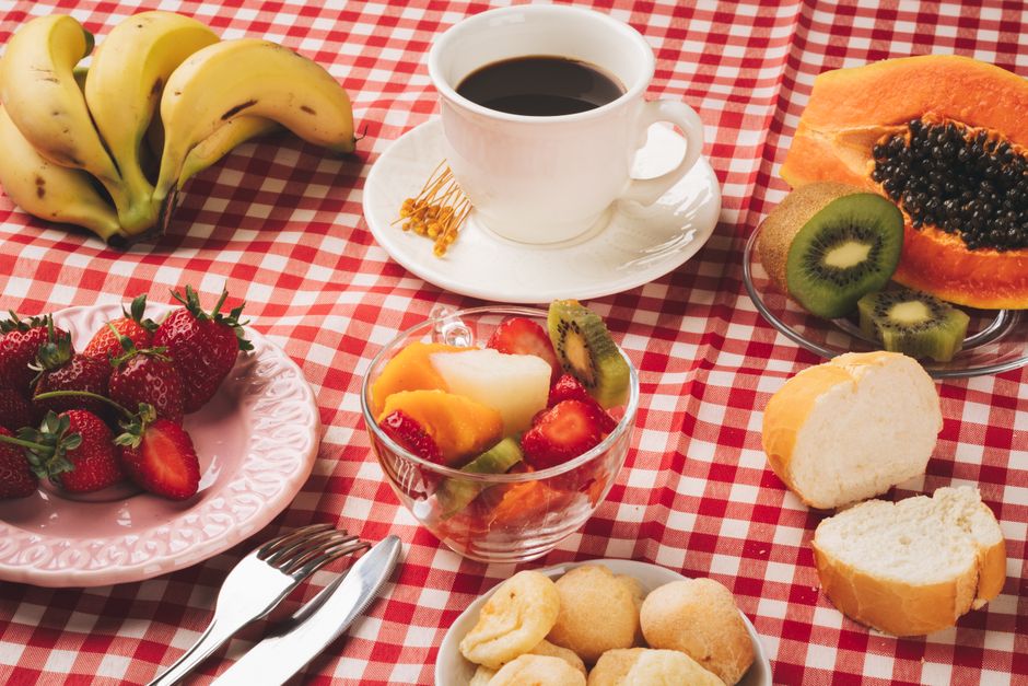 Delicious breakfast table with coffee, fresh fruits, and bread on a checkered tablecloth.