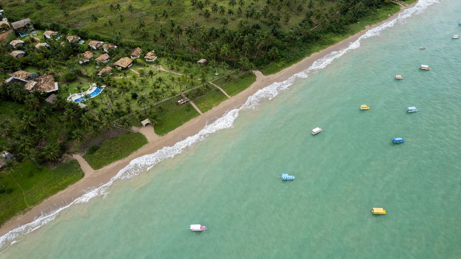 Stunning aerial view of Porto de Pedras shoreline with boats and tropical trees.