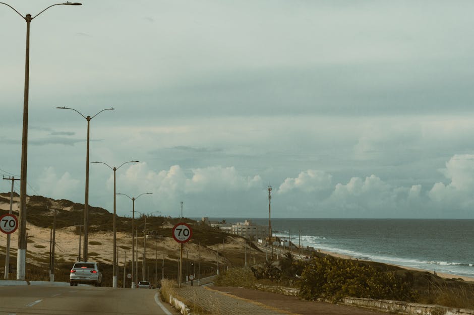 Coastal road scene with sandy dunes and ocean view in Natal, Brazil at daytime.