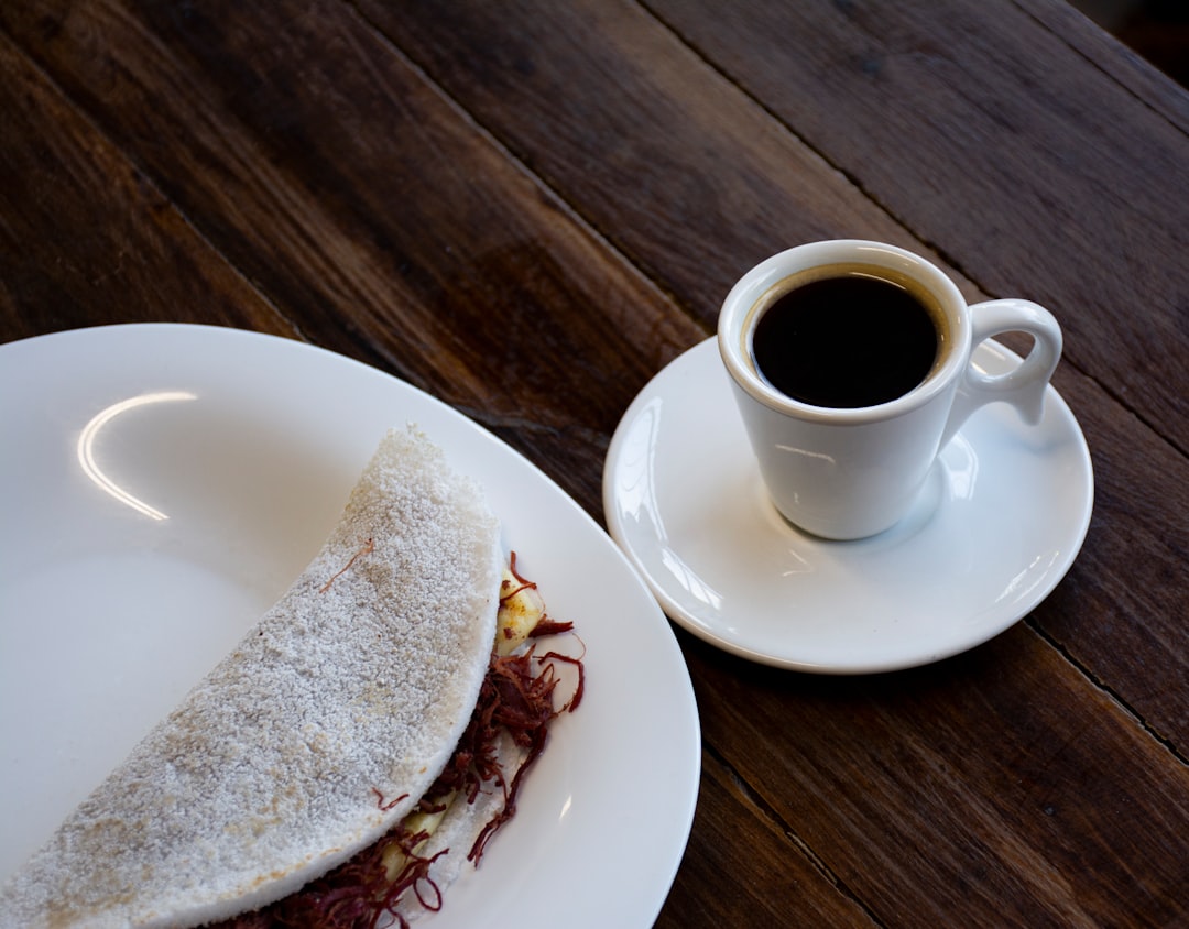 a white plate topped with a sandwich next to a cup of coffee