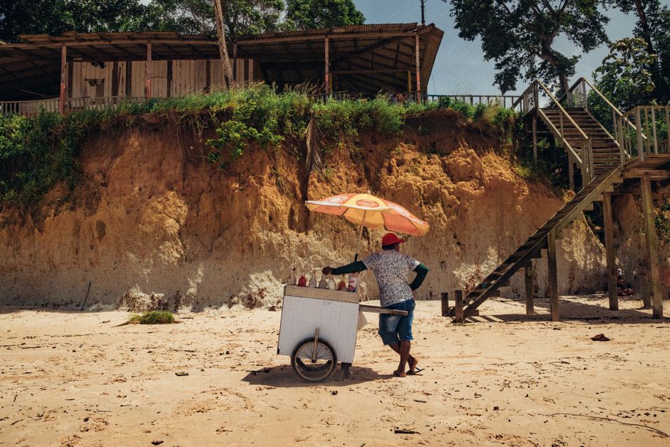 A beach vendor with an ice cream cart under an umbrella at Nazaré Beach, Brazil.