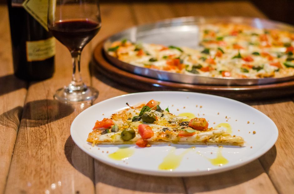 A slice of gourmet pizza with wine on a wooden table, showcasing a perfect dining atmosphere.
