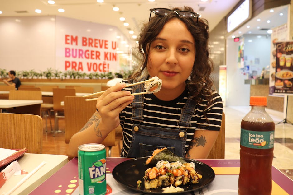 Young woman savoring sushi with chopsticks in a vibrant food court.