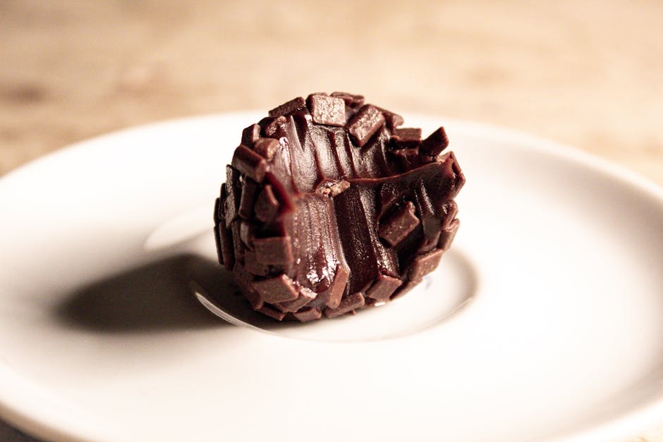 Elegant chocolate truffle artfully presented on a sleek white saucer, perfect for dessert lovers.