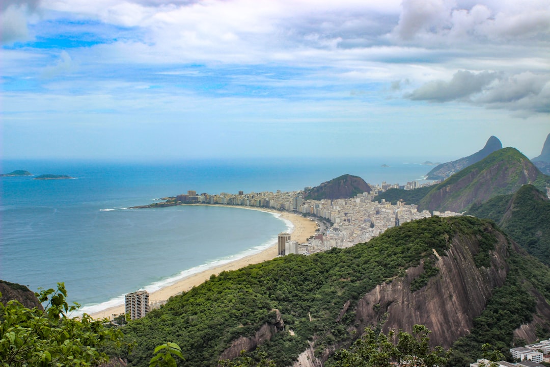 mountains and buildings near body of water under white clouds at daytime