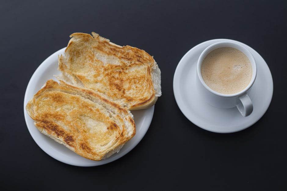 A cup of coffee with toasted bread on a black surface, ideal breakfast setting.